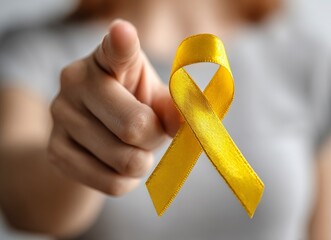 Close-up photo of a yellow ribbon on a woman's hand, pointing a finger. This image represents cancer awareness and was the winner of a stock photo contest.