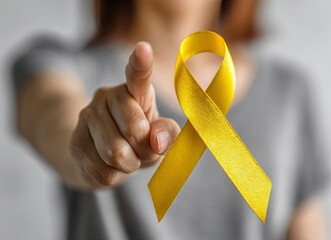Close-up photo of a yellow ribbon on a woman's hand, pointing a finger. This image represents cancer awareness and was the winner of a stock photo contest.