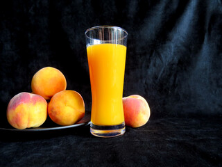 Peach juice in glass with peaches on black background. Healthy summer drink, organic fruit beverage concept.