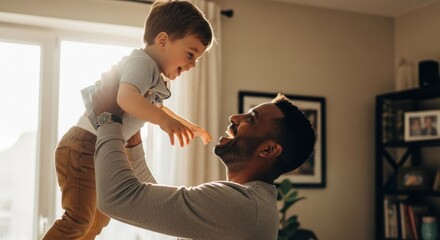 Father joyfully lifts his young son in the air indoors, sunlit background