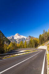 Fototapeta premium Winding mountain road leading to the Dolomites in autumn with a clear blue sky
