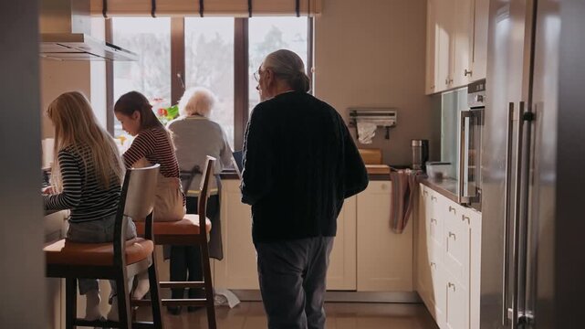 Grandpa walks into the kitchen while holding a folder and watching his granddaughter roll out the dough