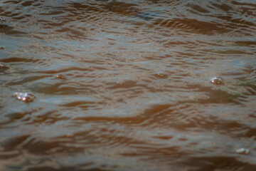 A detailed view of brownish water with small surface bubbles and natural light reflections creating fluid patterns.