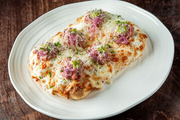 Flatbread topped with melted cheese, meatballs, pickled onions, grated cheese, and parsley, served on a white plate over rustic wooden background