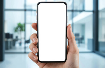 Hand holds smartphone with white blank screen for product presentation. Mobile device in fingers on blurred office background. Cellphone display template for application, web design.