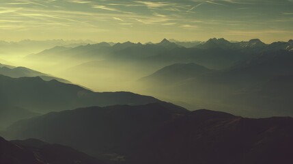 Obraz premium A vast mountain range stretches out, bathed in the soft, golden light of dawn, with layers of mist creating an ethereal atmosphere.