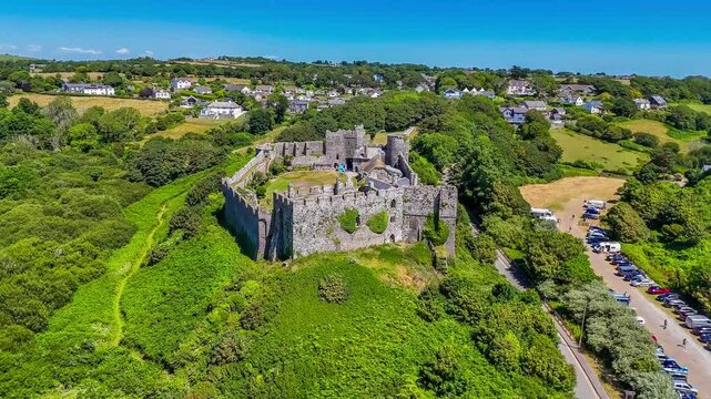 A receding aerial view towards the old Norman castle ruins at the seaside resort of Manorbier, South Wales in summertime