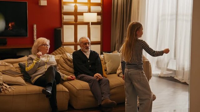 Grandfather, grandmother, and granddaughter are sitting on the couch and guessing what her sister is showing across from them