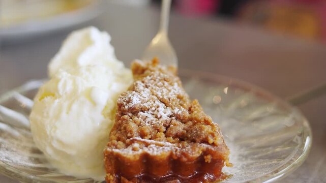 Selective focus, close-up shot of a fork lifting a bite of warm apple crumble pie served with a scoop of creamy vanilla ice cream showing delicious dessert for food, cafes, and sweet treats.