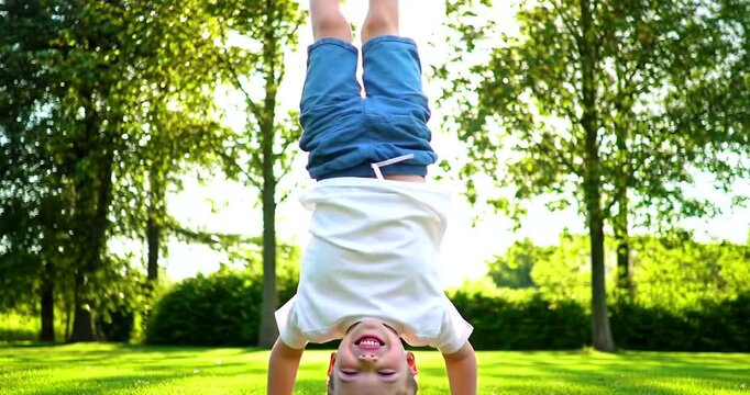 Young boy doing a handstand on the grass in a park on a sunny day