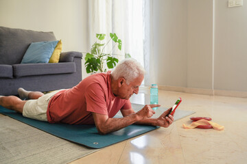 Senior man Elderly man exercising on yoga mat at home following workout instructions on his smartphone