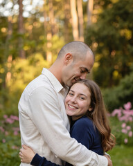 Fototapeta premium Father hugs happy teenage daughter in wooded park during late afternoon. Family bond, love, joy expressed through warm embrace. Outdoor portrait captures cheerful moment between man and girl.