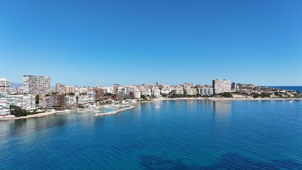 Obraz premium Panoramic view of a coastal city with modern buildings, sandy beach and clear blue sea under a bright sunny sky.
