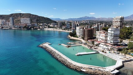 Obraz premium Panoramic view of a coastal city with modern buildings, sandy beach and clear blue sea under a bright sunny sky.