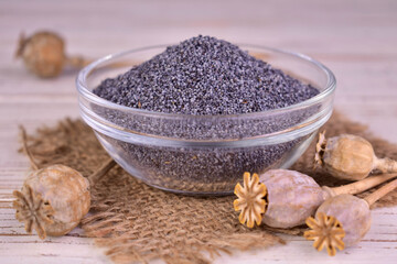 Poppy seeds in a transparent bowl and dried poppy heads, on a white background.	