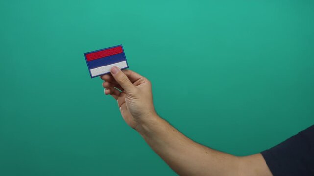 Man holding embroidery patch of russian flag against a vibrant green wall background, showcasing national pride.