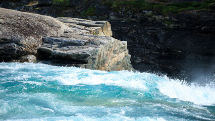 Close up of the sapphire blue water running down the big rock in D&oslash;nfoss river in summer Norway