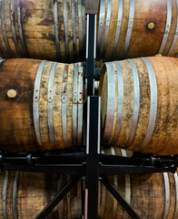 Many oak barrels for storing wine or whiskey stacked in dark cellar. Winery production process and aging concept. Big round wine cellar for storage of alcoholic beverages placed inside modern factory
