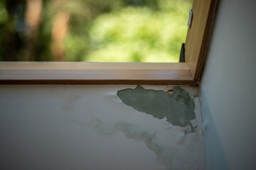 Peeling paint and stains reveal water damage on a wall beneath a wooden window frame, caused by moisture intrusion.