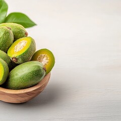 A wooden bowl overflows with fresh feijoa fruit, some sliced to reveal the juicy yellow flesh, creating a delightful and healthy still life arrangement.