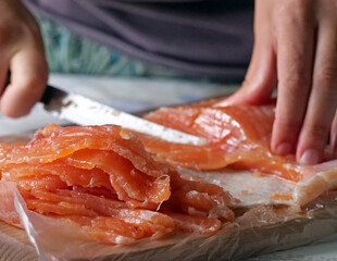 Hands slicing a salmon fillet - A Person Methodically Slicing a Large Fillet of Smoked Salmon into Thin Pieces