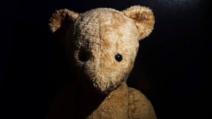 old teddy bear on black background, portrait lighting
