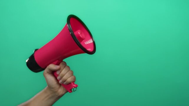 Hand holding pink megaphone against green background conveying communication and announcement concept.