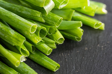 Fresh green spring onions on black stone background, closeup, horizontal.