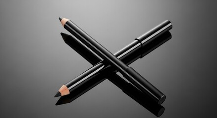 Two black eyeliner pencils crossed on a reflective dark surface, highlighting their sharp tips and sleek design