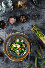 Delicious spring salad with asparagus, peas, gnocchi and mozzarella cheese seasoned with spices on dark background
