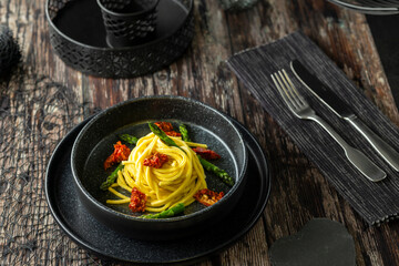 Delicious spaghetti with asparagus and dried tomatoes served on black plate