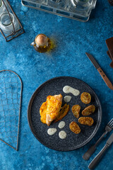 Chicken cordon bleu with potatoes and white sauce on blue background