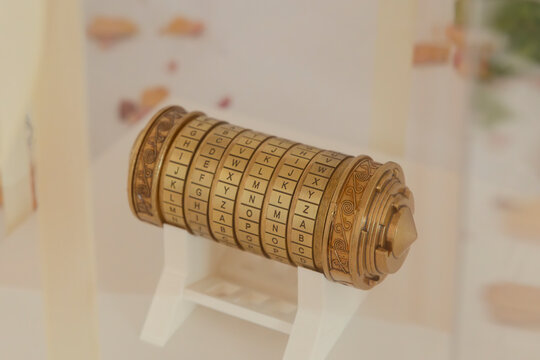 Cryptex combination lock showing alphabet letters on rings, placed on white support