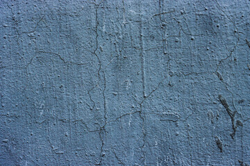 Concrete wall with worn blue paint and cracks.