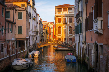 Venetian canal with footbridge and boats at sunset