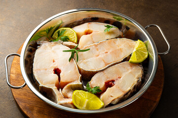Raw catfish steaks with herbs, lime and spices in a baking dish on a dark background