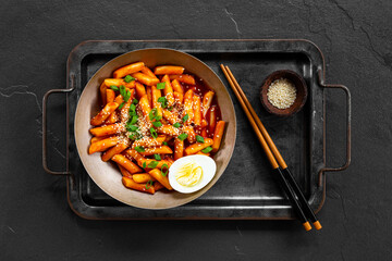 Korean street food, tteokbokki with egg and sesame on dark background top view