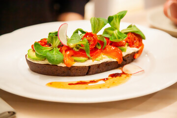 Colorful open-faced sandwich topped with fresh vegetables and herbs at a cozy restaurant