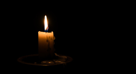 Illuminated candle on plate against dark background  