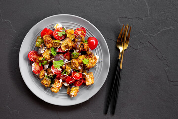  Georgian salad with deep fried eggplant, tomatoes, onions, feta cheese and cilantro on the dark background. Vegetarian food with eggplant and other vegetables, top view
