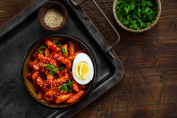 Korean street food, tteokbokki with egg and sesame on dark wooden background