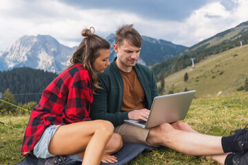 Happy campers couple enjoying a relaxing getaway, connecting with nature and having fun via laptop,...
