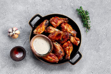 Fried chicken wings with sauce on black plate and grey background top view