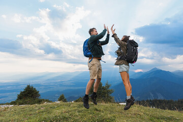 Two hikers joyfully high-five at the summit after reaching their destination, surrounded by...