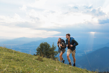 Young couple geared with backpacks, hiking uphill in the mountains at dusk, experience adventure in the great outdoors.