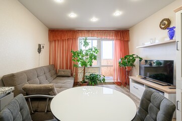 cozy living room featuring a sofa, round table, TV, and lots of plants. Warm tones and good lighting give it an inviting feel
