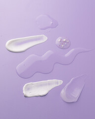 Different textures of skincare and cosmetic products including cream, gel, and lotion smeared on a pastel purple background. Beauty and self-care concept showcasing product texture variety, 