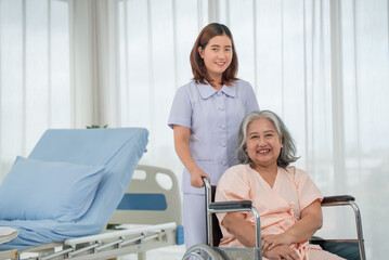 Fototapeta premium Asian nurse pushing senior female patient in a wheelchair at the hospital ward