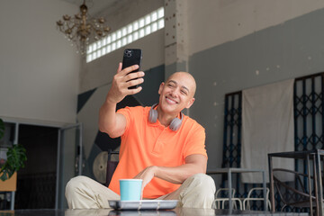 Man with coffee using phone in cafe restaurant wearing orange polo shirt having video call meeting