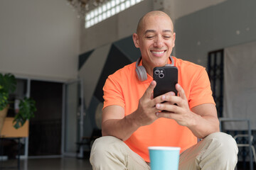 Bald Hispanic man with smiling and texting with phone in coffee shop during morning